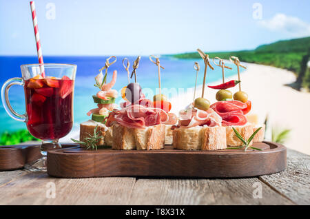 Set of Spanish tapas served on a sliced baguette with sangria on wooden table against the sea Stock Photo