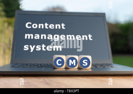Dice form the abbreviation "CMS". Dice placed on a Notebook. The text "Content management system" is written on the display. Stock Photo