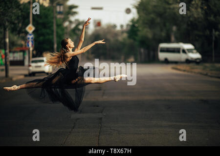 Ballerina jumping in twine pose in a black transparent dress against the background of city street. Stock Photo