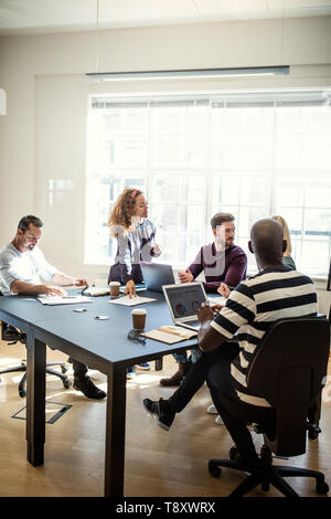 Group of diverse designers sitting around a boardroom table in an office working together on a project Stock Photo