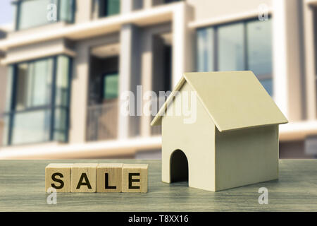 Home and real estate sale concept. A small residential model with sale wooden block on wood table on blurred real estate as background. Depicts house 