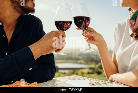 Cropped shot of a couple sitting together with a glass of wine. Side view of a couple on a date talking to each other toasting glasses of red wine. Stock Photo