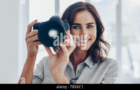 Beautiful young female photographer with dslr camera photographing. Happy woman shooting with professional camera. Stock Photo