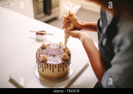 Close up of a woman decorating chocolate cake in the kitchen. Female chef decorating cake with whipped cream using piping technique. Stock Photo