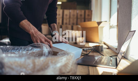 Small business owner packing in the cardbox at workplace. Cropped shot of man preparing a parcel for delivery at online selling business office. Stock Photo