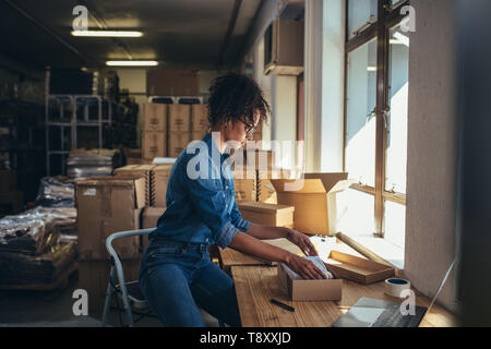 Female business owner working, packing the order for shipping to customer. Female entrepreneur packaging box for delivery. Stock Photo