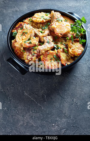 browned pork chops on bone and hash brown stew in a black ceramic pan on a concrete table, vertical view from above, Stock Photo