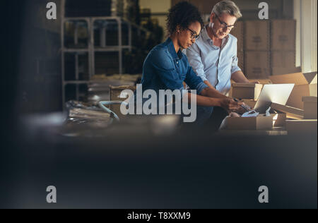 Online shop business partners working in small office together. Woman packing the purchased product in the box with man updating the shipment status o Stock Photo