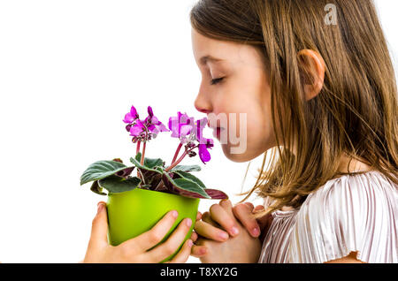 Little girl smelling viola flowers in green pot. Child is smelling flowers given as a gift or present. Profile view, studio shot, isolated on white ba Stock Photo