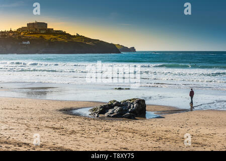 A man walking alone in the evening light on Great Western Beach in Newquay in Cornwall.