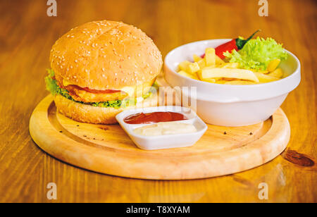 Cheat meal. Delicious burger with sesame seeds. Burger menu. High calorie snack. Hamburger and french fries and tomato sauce on wooden board. Fast food concept. Burger with cheese meat and salad. Stock Photo