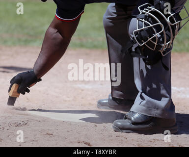 African American umpire cleaning home plate at a high school baseball game Stock Photo