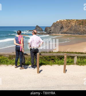 Couple standing looking out over the coastline view of headlands and bay with wide sandy beach, Praia de Odeceixe, Algarve, Portugal, Southern Europe Stock Photo