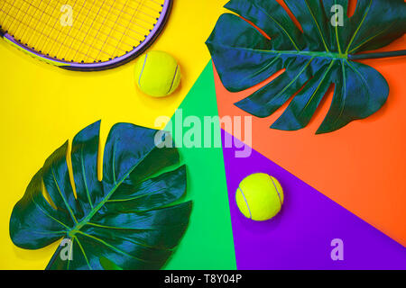 Tennis layout with tennis balls, racket and tropical monstera leaves on abstract different multicolored neon background with place for text. Stock Photo