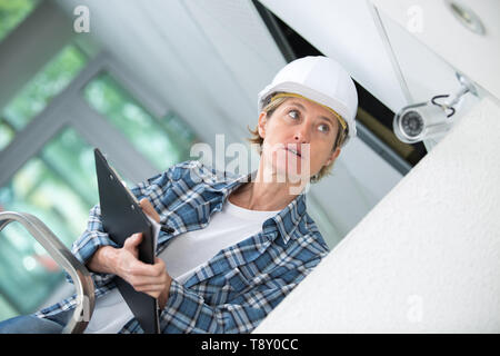female technician installing camera on wall with screwdriver Stock Photo