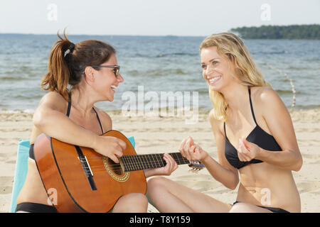 two women playing guitar on beach Stock Photo