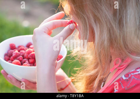 Young girl holding a plate of raspberries, sitting on green grass, summer, dessert Stock Photo