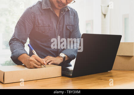 SME Business man writing address on parcel with labtop on the table. Stock Photo