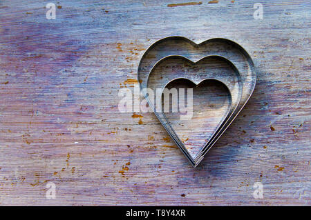 Three heart shaped metal cookie cutters, nested on a wooden background. Stock Photo