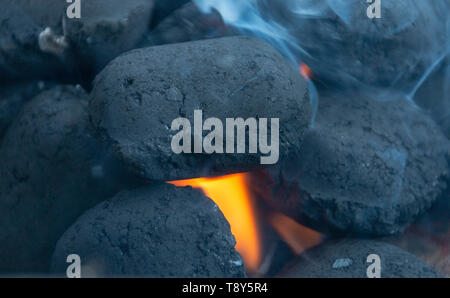 A close up view of smoke and black hot coals where the flames are peaking though Stock Photo