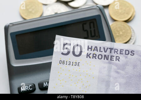 A fifty krone note over a calculator and mixed coins with selective focus. The krone is the official currency of Denmark, Greenland and Faroe Islands. Stock Photo