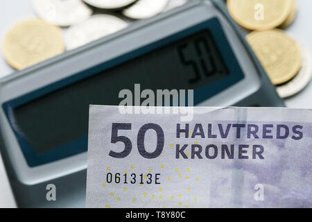 A fifty krone note over a calculator and mixed coins with selective focus. The krone is the official currency of Denmark, Greenland and Faroe Islands. Stock Photo
