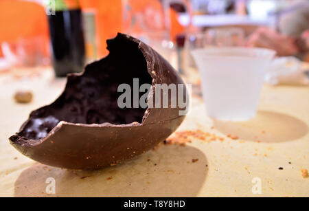 An Easter egg has been opened, the broken chocolate shell is on the table resting in its wrapping. A Caucasian man's hand cuts off a piece of food. 30 Stock Photo