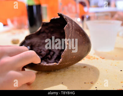 An Easter egg has been opened, the broken chocolate shell is on the table resting in its wrapping. A Caucasian man's hand cuts off a piece of food. 30 Stock Photo
