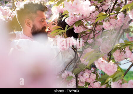 Couple in love kissing under blooming tree. Bearded man and pretty girl hiding in pink cherry blossom. Romantic date in spring flowering garden Stock Photo