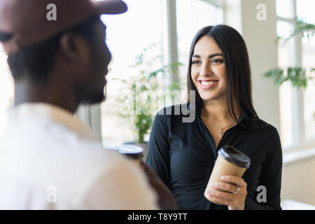Smiling mixed race colleagues in casual clothes have informal meeting while drinking coffee in modern office Stock Photo