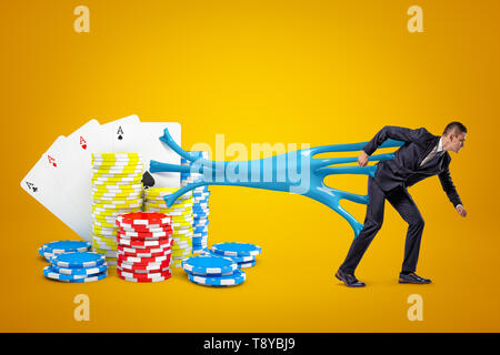 Young businessman stuck to playing cards and casino chips with blue sticky slime on yellow background Stock Photo