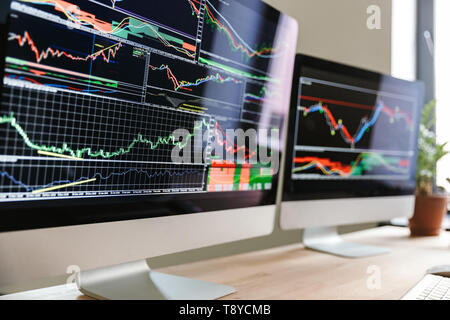 Photo of two computer monitors with colorful graphics and charts standing on table in bright office Stock Photo