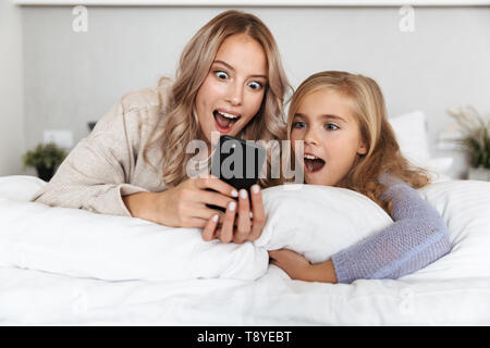 Image of two shocked girls sisters on bed in bedroom at home posing ...