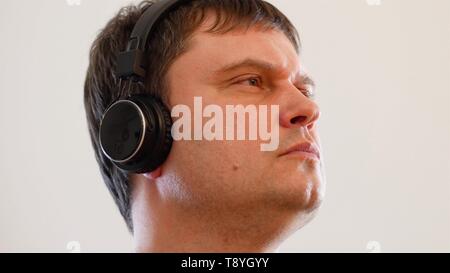 Millenial young man wearing wireless black headphones rocking out to music and smile singing along, on a white background. The middle aged caucasian m Stock Photo