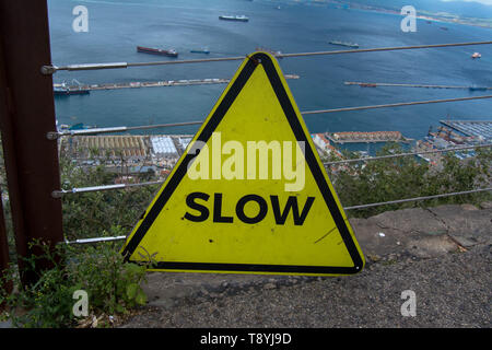 Slow sign on Gibraltar rock overlooking the sea triangle painted yellow view of the sea and boats boat water sea danger dangerous hill cliff calm seas Stock Photo