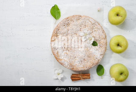 Flat lay with tasty apple pie, apples , spring  flowers , leaves and cinnamon sticks. Homemade round apple pie on the parchment paper with icing sugar. Stock Photo