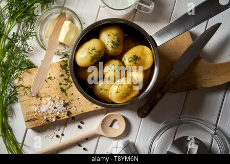 Young potatoes boiled in  pot with dill and butter on wooden board Stock Photo