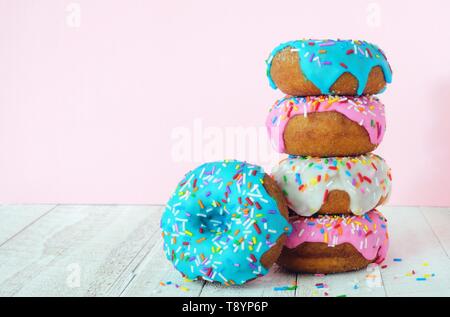 Stack of donuts with pastel colored icing on a soft pink background