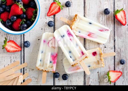Group of homemade mixed berry yogurt popsicles. Top view on a rustic white wood background. Stock Photo