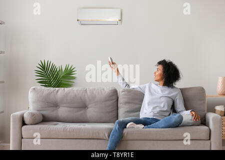 Smiling African American woman using air conditioner remote controller Stock Photo