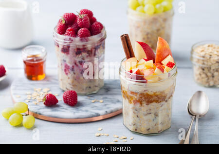 Overnight oats, bircher muesli with raspberry, apple in glass jars on wooden background. Stock Photo
