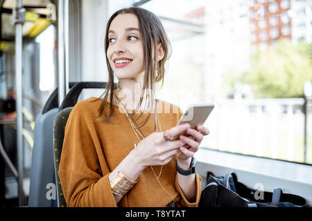 Young and happy woman using smartphone while sitting near the window in the public transport during the trip Stock Photo