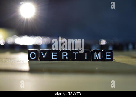 OVERTIME concept wooden blocks on the table. With personal development and motivation concept on blurred or black background Stock Photo