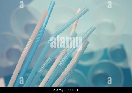 Blue and white plastic tubules in front of plastic cups. Polymers in everyday life. Problem of plastic pollution in environment. Conceptual. Selective Stock Photo