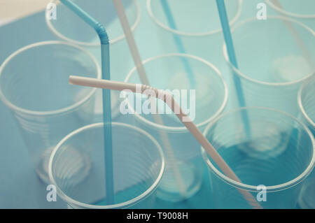 Disposable plastic cups on a blue and white background. Plastic straw tubules inside cups. Selective focus. Light tone. Concept of plastics. Stock Photo