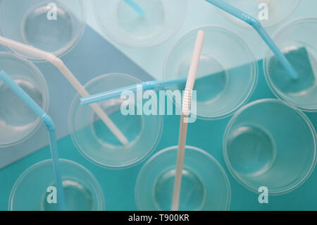 Disposable plastic cups with straws tubules on white and turquoise background. Concept of plastics. Selective focus. Top view. Bright and light tone. Stock Photo