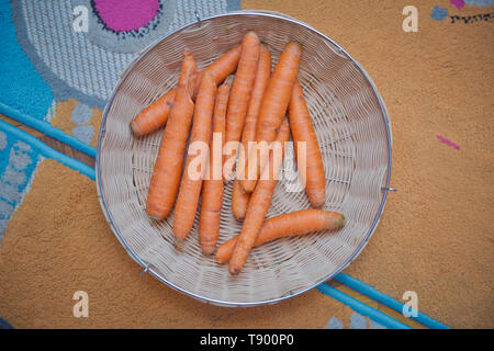 fresh baby in basket . Young brightly orange carrots, fresh with tops of vegetable, in a wicker basket. Spring harvest. The root is in the basket . Stock Photo
