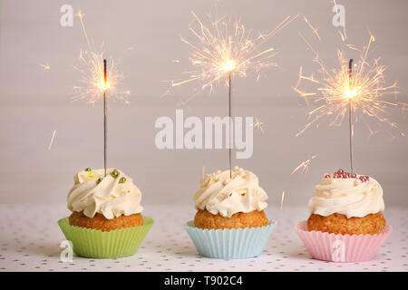 Sweet tasty cupcakes with burning sparklers on light table Stock Photo