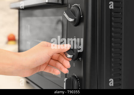 Woman adjusting electric oven in kitchen Stock Photo
