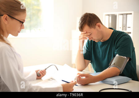 Female doctor measuring blood pressure of male patient in hospital Stock Photo